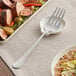 An Acopa stainless steel serving fork next to a plate of food with meat and vegetables.