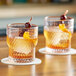 Two Acopa Rivulet stackable rocks glasses with whiskey and cherries on a table.