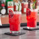 Two Acopa stackable beverage glasses filled with red liquid and a rosemary sprig on a table.