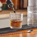 A person pouring whiskey into an Acopa Rivulet old fashioned glass on a counter in a cocktail bar.