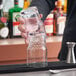 A hand pouring a drink into a stack of Acopa Rivulet beverage glasses on a table.