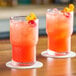 Two Acopa stackable beverage glasses filled with red liquid and ice with orange slices on a table.