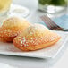 Two White Toque individually wrapped madeleines on a white plate with a fork.