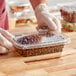 A gloved hand holding an Inline Plastics rectangular plastic container of beans.