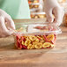 A hand holding an Inline Plastics rectangular plastic container filled with fruit and nuts.