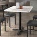 A Lancaster Table & Seating rectangular table with a white marble finish on a black metal base.