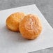 Two White Toque plain mini beignets on a white paper.