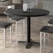 A Lancaster Table & Seating round black thermo-formed MDF table top on a table with chairs in a restaurant dining area.