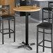 A Lancaster Table & Seating round bar table with a maple finish and two black chairs.