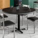 A Lancaster Table & Seating round table with a black wood finish and chairs with salt and pepper shakers on top.