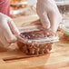 A gloved hand holding an Inline Plastics Safe-T-Fresh square deli container of chocolate candies.