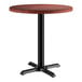 A Lancaster Table & Seating round table with a red mahogany finish on a black base.