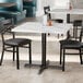 A Lancaster Table & Seating white marble table top on a table with black chairs.