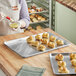 A woman wearing a white apron putting food into a Nordic Ware aluminum sheet pan.