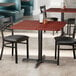 A Lancaster Table & Seating square table in a restaurant with a red mahogany finish.