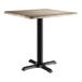 A square standard height table with a gray wood finish top and a black metal pedestal base.