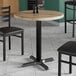 A Lancaster Table & Seating round thermo-formed MDF table top with a gray wood finish on a table with black metal legs.