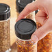 A hand holding a black 48/485 polypropylene spice cap over a jar of spices.