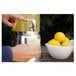 A hand pouring yellow liquid from a dispenser into a Tossware taster glass.