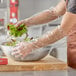 A person wearing Choice elbow-length plastic gloves preparing salad in a bowl.