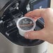 A hand holding a Peet's Coffee Major Dickason's Blend K-Cup pod over a Keurig machine.