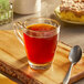 A glass mug of Caribou Coffee Daybreak Morning Blend tea on a wooden board with a spoon.