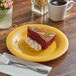 A piece of cake with whipped cream on a yellow Acopa Foundations melamine plate with a cup of coffee and a glass of coffee.