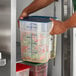 A person holding a Cambro FreshPro translucent square polypropylene container with food inside.