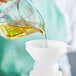 A hand pouring Mazola Corn Oil from a funnel into a measuring cup.
