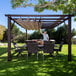 A man standing under a Paragon Outdoor Modena aluminum pergola with a table and chairs on a lawn.