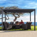 A man and woman sitting at a table under a Paragon Outdoor Novara louvered pergola.