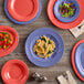 An orange Acopa Foundations melamine platter with food on a wood table.