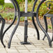 A Lancaster Table & Seating black steel bolt-down umbrella base on a patio table with two chairs and an umbrella.
