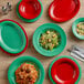 A wood table topped with a stack of Acopa red melamine platters with a green salad on one plate.