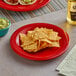 A red Acopa Foundations melamine plate with chips and guacamole on a table.