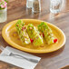 A yellow Acopa Foundations wide rim melamine platter with food on a table.