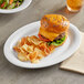 An Acopa white melamine platter with a cheeseburger and chips on it.