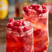 Two glasses of red raspberry cocktails garnished with raspberries.