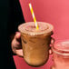 Two hands holding plastic cups with Tossware flat lids and straws.