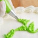 A person using a Wilton #352 leaf piping tip to pipe green icing on a cake.