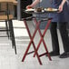 A person holding a Lancaster Table & Seating mahogany wood folding tray stand with food on it.