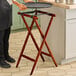 A person holding a tray on a Lancaster Table & Seating mahogany wood folding tray stand.