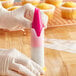 A person holding a pink and white plastic container with a pink top filled with Wilton 1M plastic piping tips.