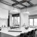 A white kitchen with a Globe brass pendant light over a large island and black chairs.