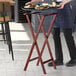 A person using a Lancaster Table & Seating mahogany wood folding tray stand to hold a tray of food.