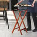 A person using a Lancaster Table & Seating walnut wood folding tray stand to hold a tray of food.