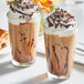 Two glasses of coffee with whipped cream and Guittard dark chocolate sauce on a table.