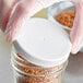 A person in gloves holding a jar of food with a white ribbed plastic cap.