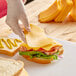 A person in gloves cutting Tillamook medium yellow cheddar cheese on a counter.