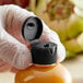 A gloved hand using a black 24/410 flip top lid to dispense yellow liquid from a plastic bottle.